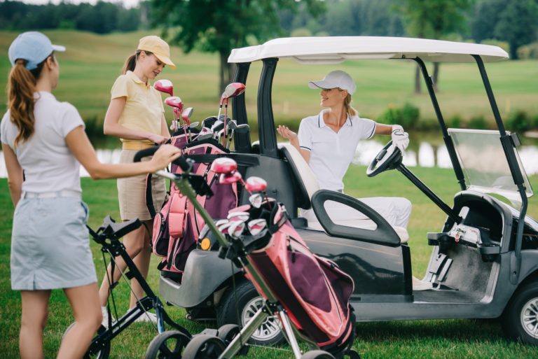 female golf players in caps at golf cart on golf course