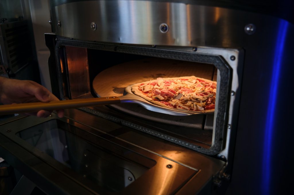Pizza oven with the door open while putting in a pizza